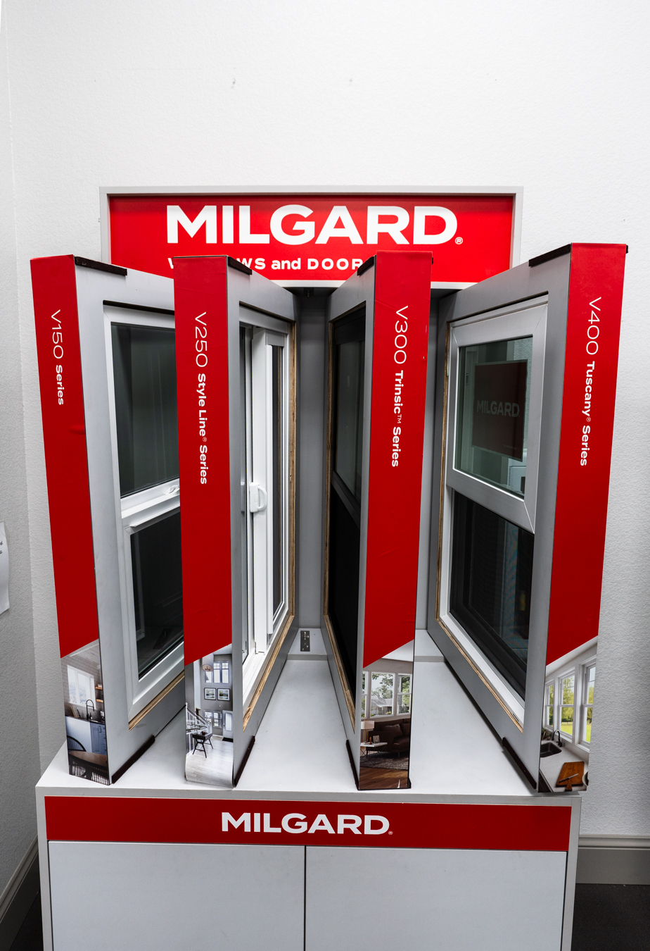 Milgard window display at Builders FirstSource, showcasing V150, V250, V300, and V400 series with red accents and frames.