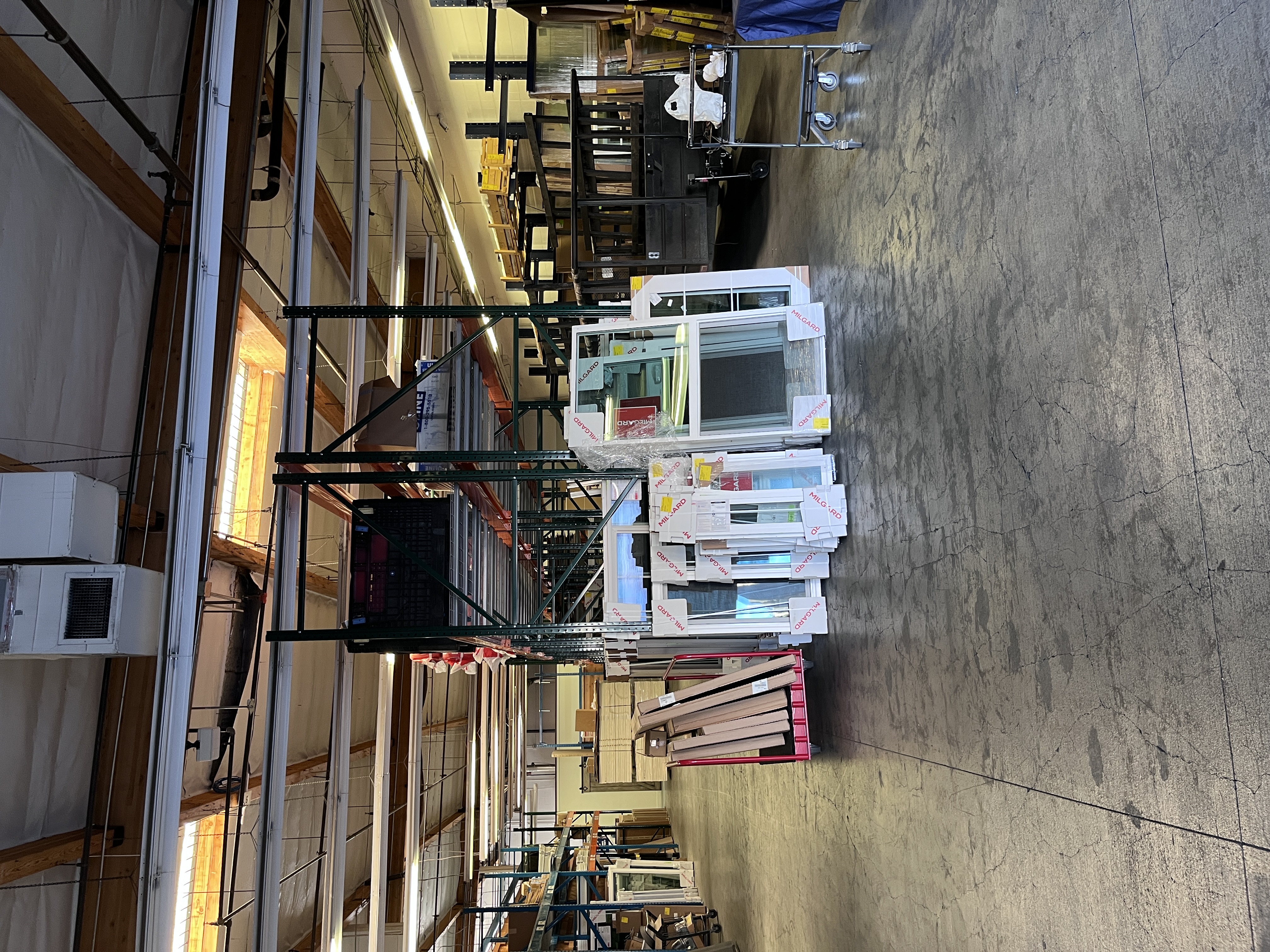 Interior warehouse storage area at Builders FirstSource Thousand Oaks, CA, showing Milgard window units staged on carts alongside lumber and material racks.
