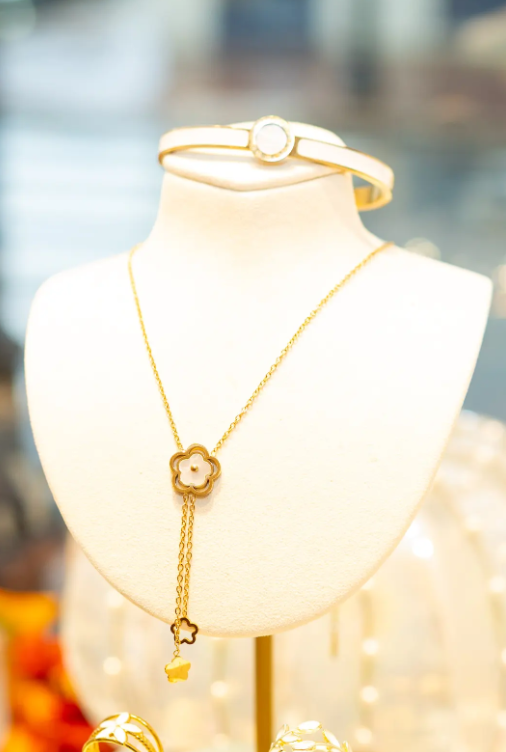 A gold-tone floral necklace with dangling charms pairs with a white-accented bangle at Eliana Curated. Explore elegant accessories to complement your individual style in Old Town Alexandria, Virginia.