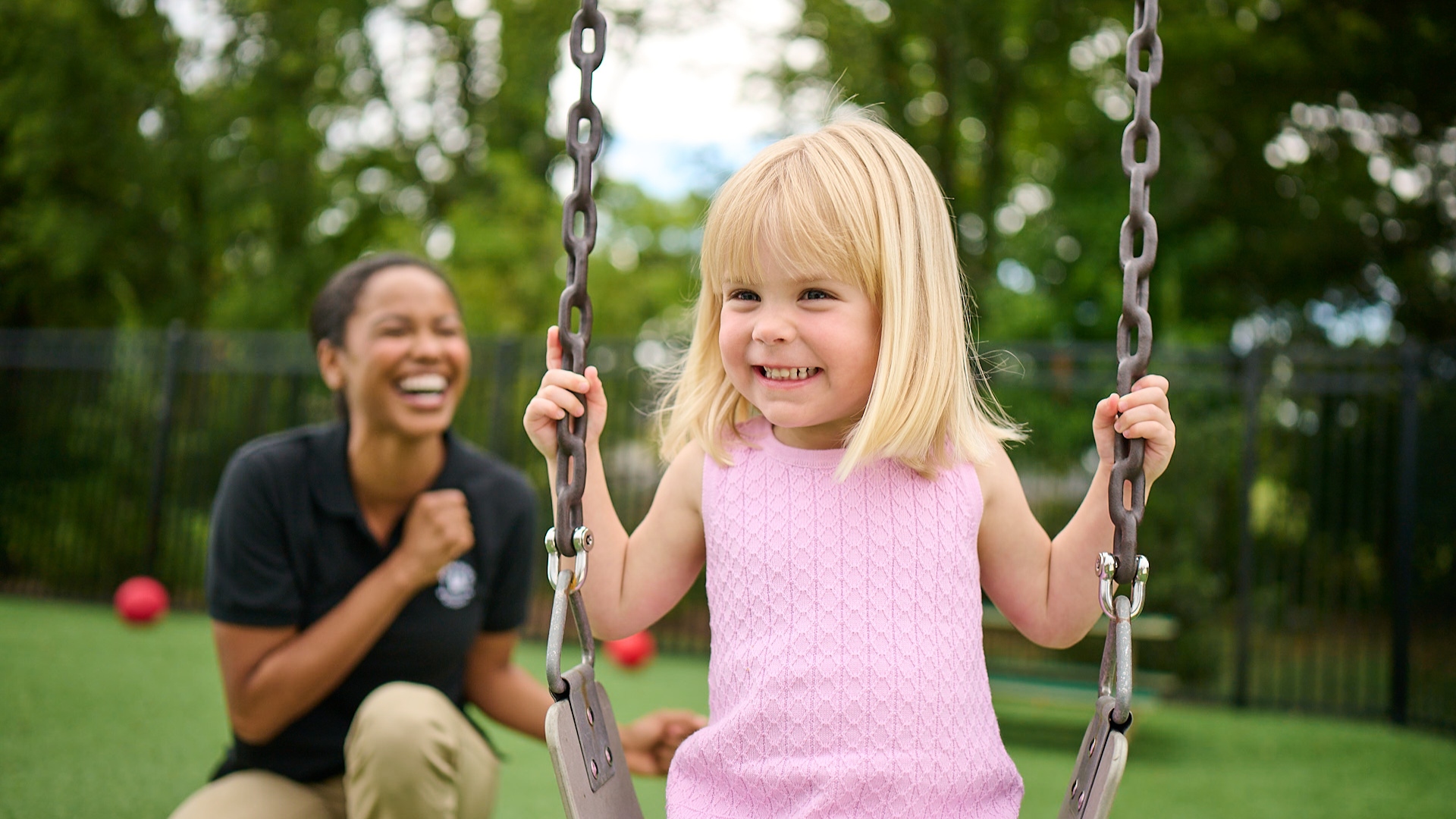 Primrose Schools teacher encouraging young girl on playground swing during outdoor play at childcare center