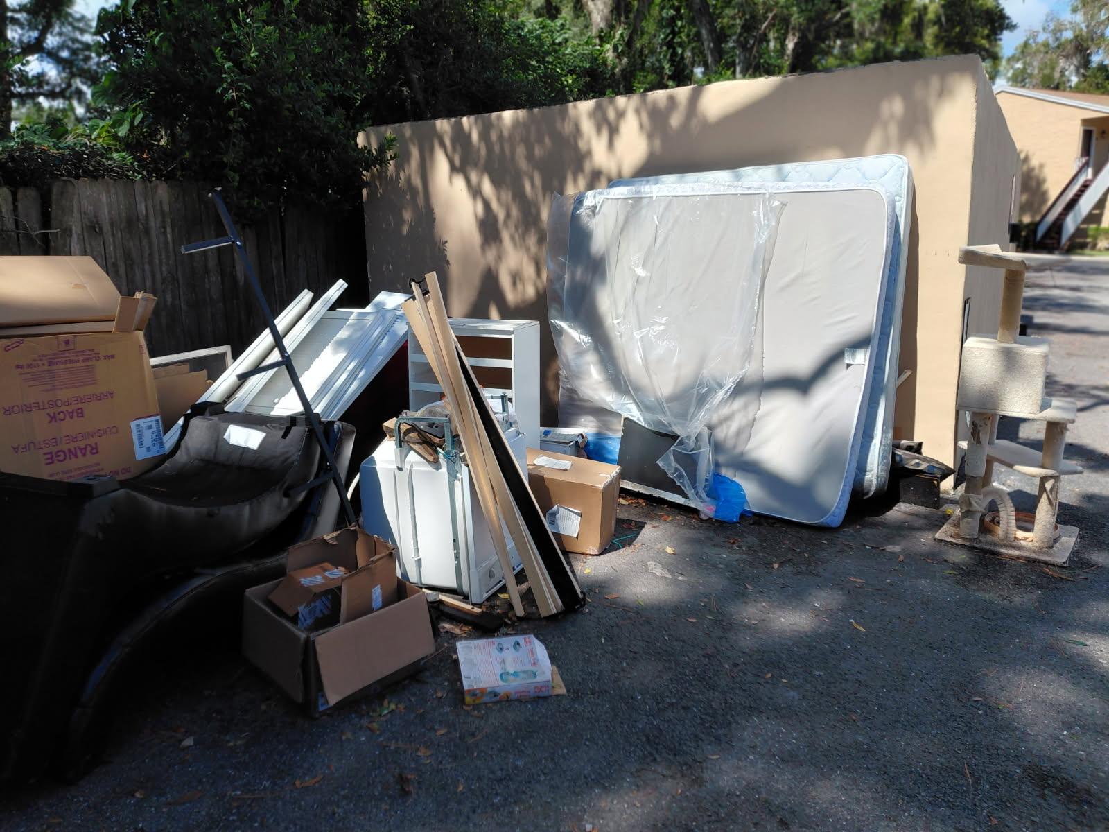 A pile of discarded property items stacked against an exterior wall, including mattresses wrapped in 