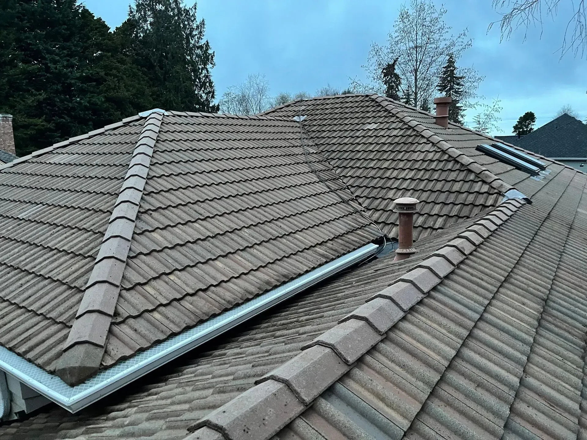 A residential roof covered with terracotta-style tiles. A new silver-colored gutter system has been installed on the lower edge. Two skylights are visible on the right side of the roof.