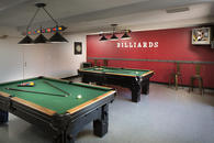 Billiards room with two billiards tables and overhead lights.