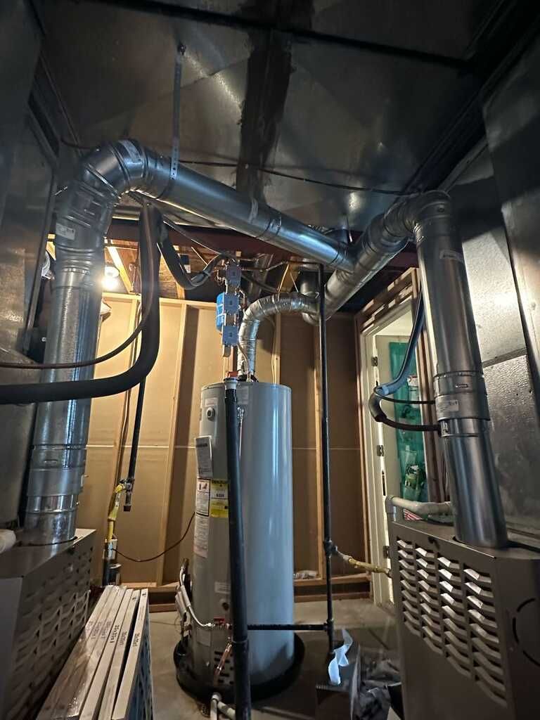 Mechanical room shows a tall tank water heater surrounded by large metal vent ducts, insulated pipes 