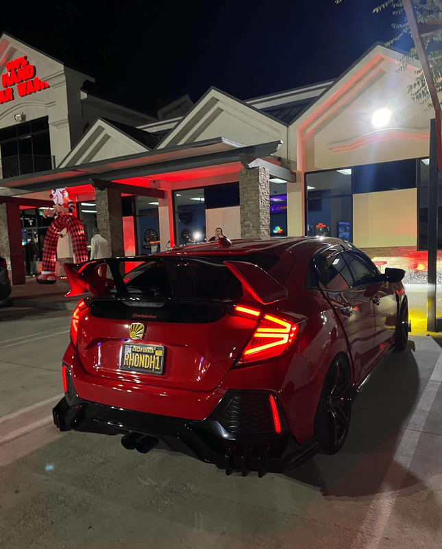 Red customized Honda Civic hatchback parked beneath bright storefront lighting during a nighttime au 