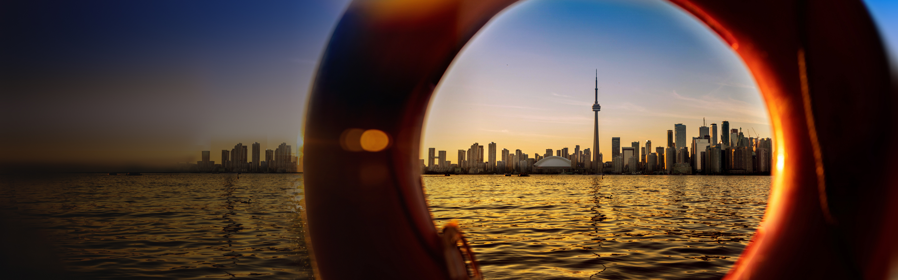 The Toronto skyline at sunset, seen from across Lake Ontario and pictured through an orange lifebuoy.