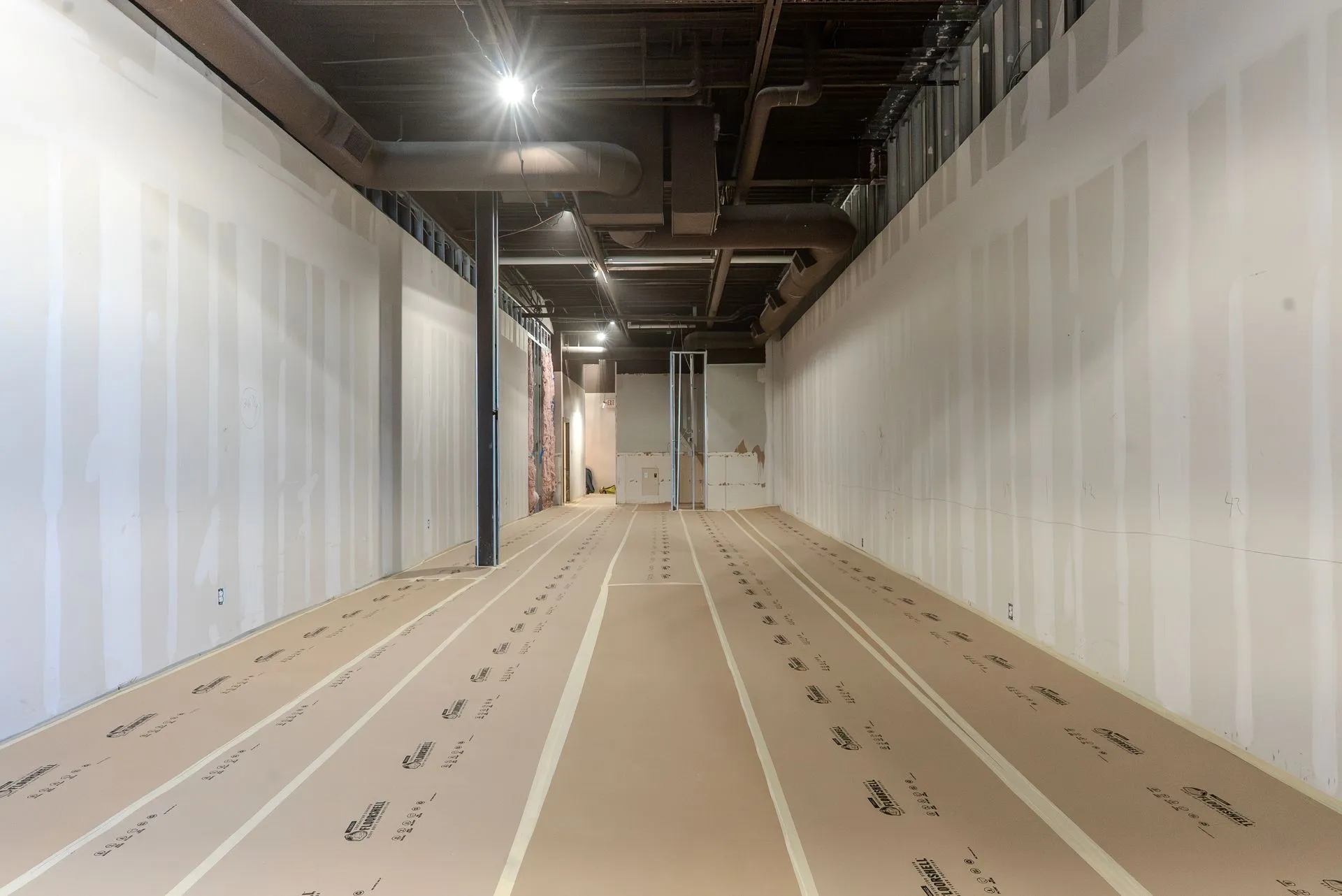 Spacious commercial interior under construction featuring newly installed drywall, exposed black cei 
