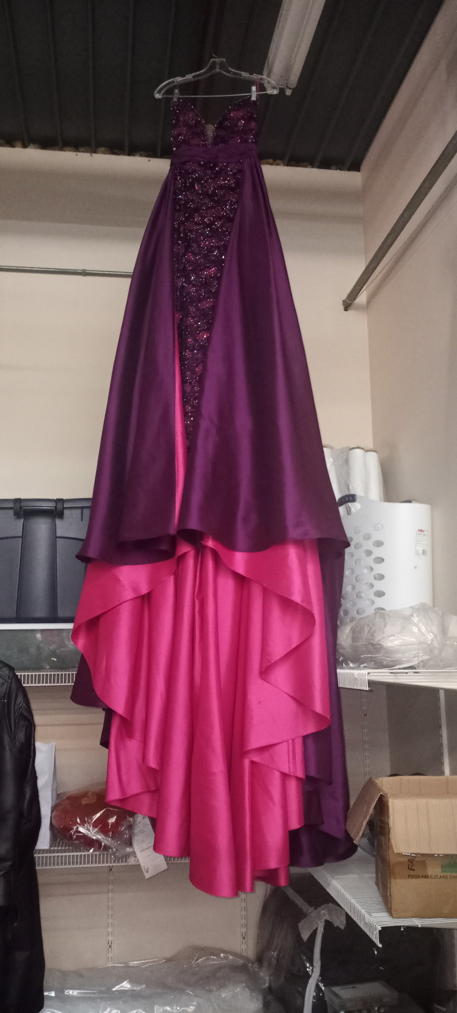 A striking purple and pink high-low evening gown with detailed bodice embellishments hanging on display at Plaza Cleaners.