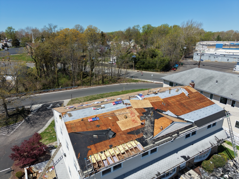 Extensive roofing renovation underway on a residential building. Crews replace damaged sections, ins 