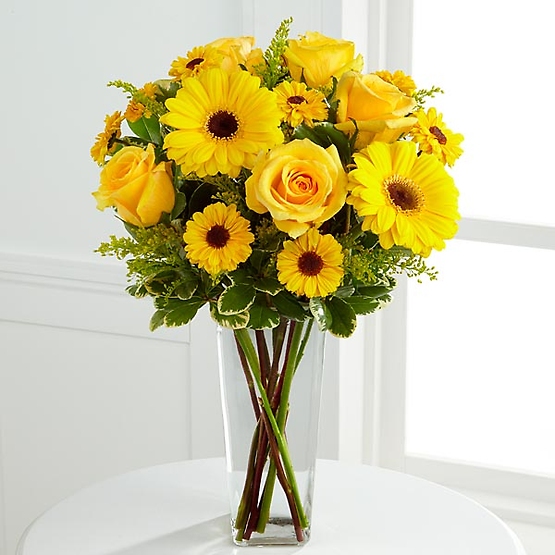 The Daylight™ Bouquet bursts with sun-filled excitement and cheer expressed through each radiant bloom. Gorgeous yellow roses and gerbera daises are accented with the golden hues of Viking chrysanthemums and solidago arranged with lush greens in a clear glass square tapered vase to create a splendid way to brighten their day.