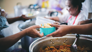 Close-up of hands giving and receiving a bowl of food at a soup kitchen.
