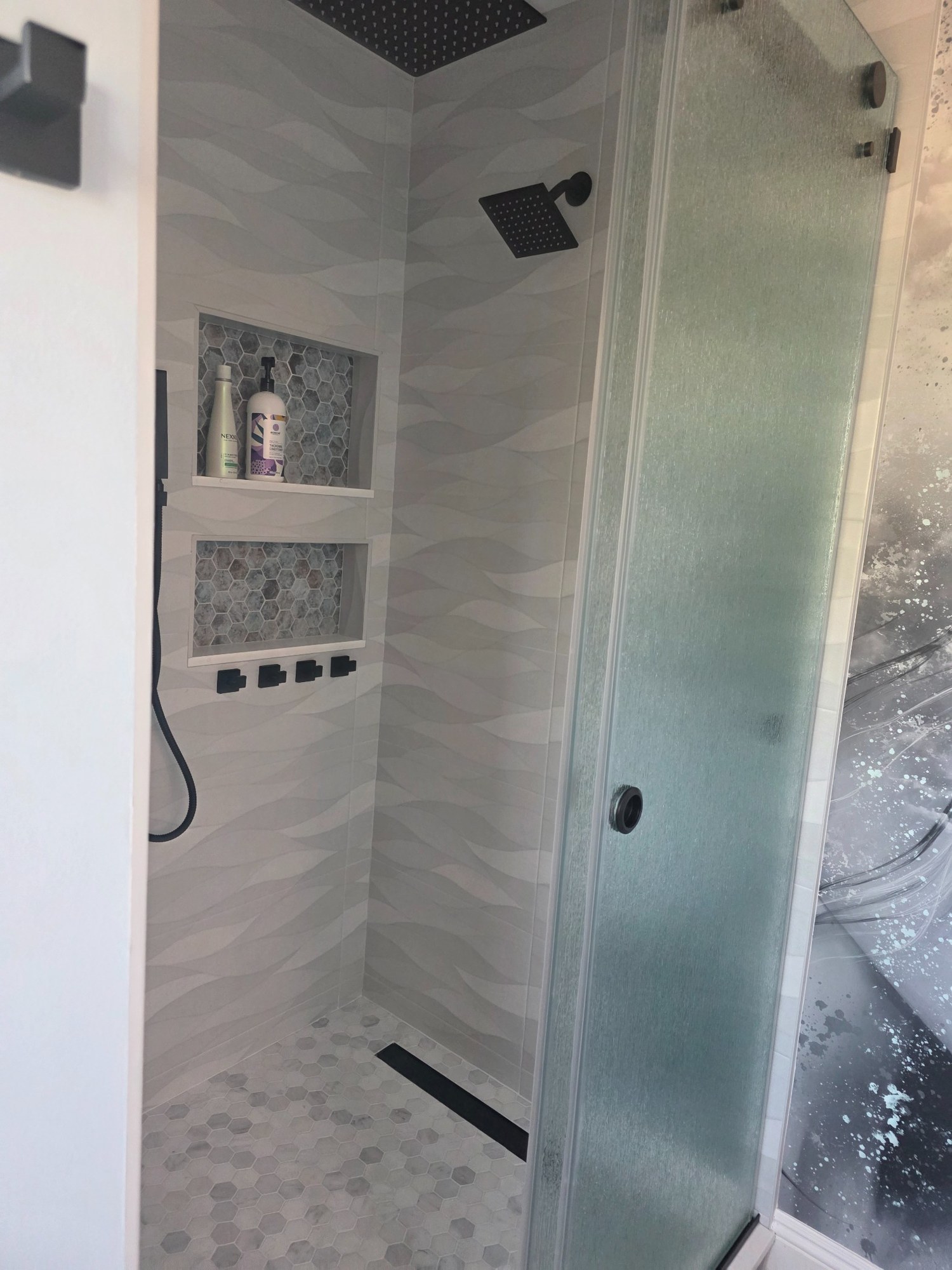 Walk-in shower remodel with tile walls, glass enclosure, and built-in controls. 