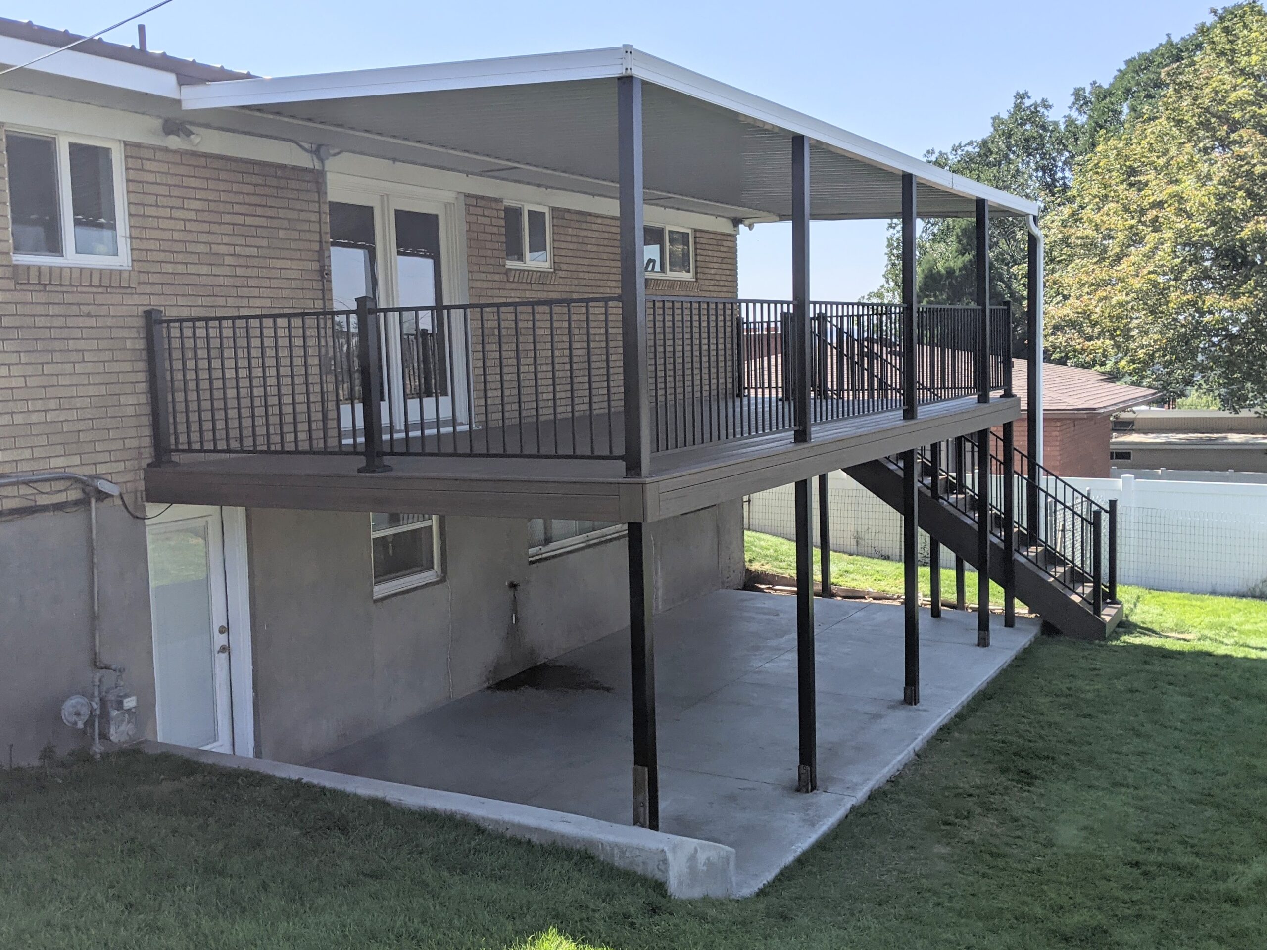 This recent project by DeckPro LLC showcases a durable second-story composite deck featuring sleek black metal railing. The design not only provides a beautiful upper-level outdoor space but also creates a functional, shaded concrete patio area underneath.