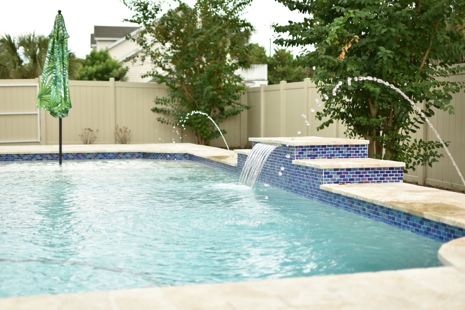 Backyard swimming pool with a raised spa, decorative blue tile, water features, and surrounding landscaping.