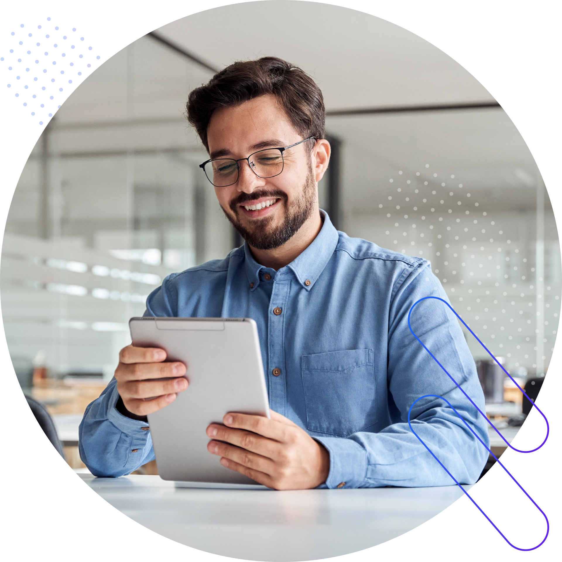 A smiling man wearing glasses and a blue button-down shirt is looking down at a tablet he is holding. He is sitting at a white desk in an office environment. The image is framed within a circle and features abstract graphical elements with polka dots and blue lines.