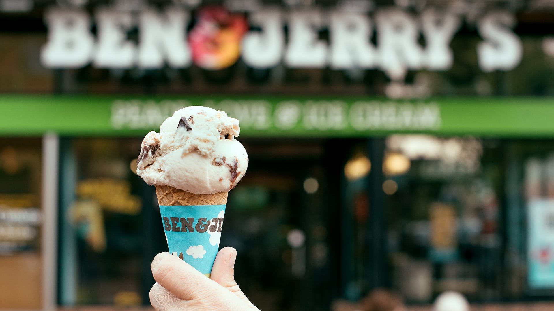 A hand holds up Ben & Jerry's Chocolate Chip Cookie Dough Ice Cream in a Waffle Cone
