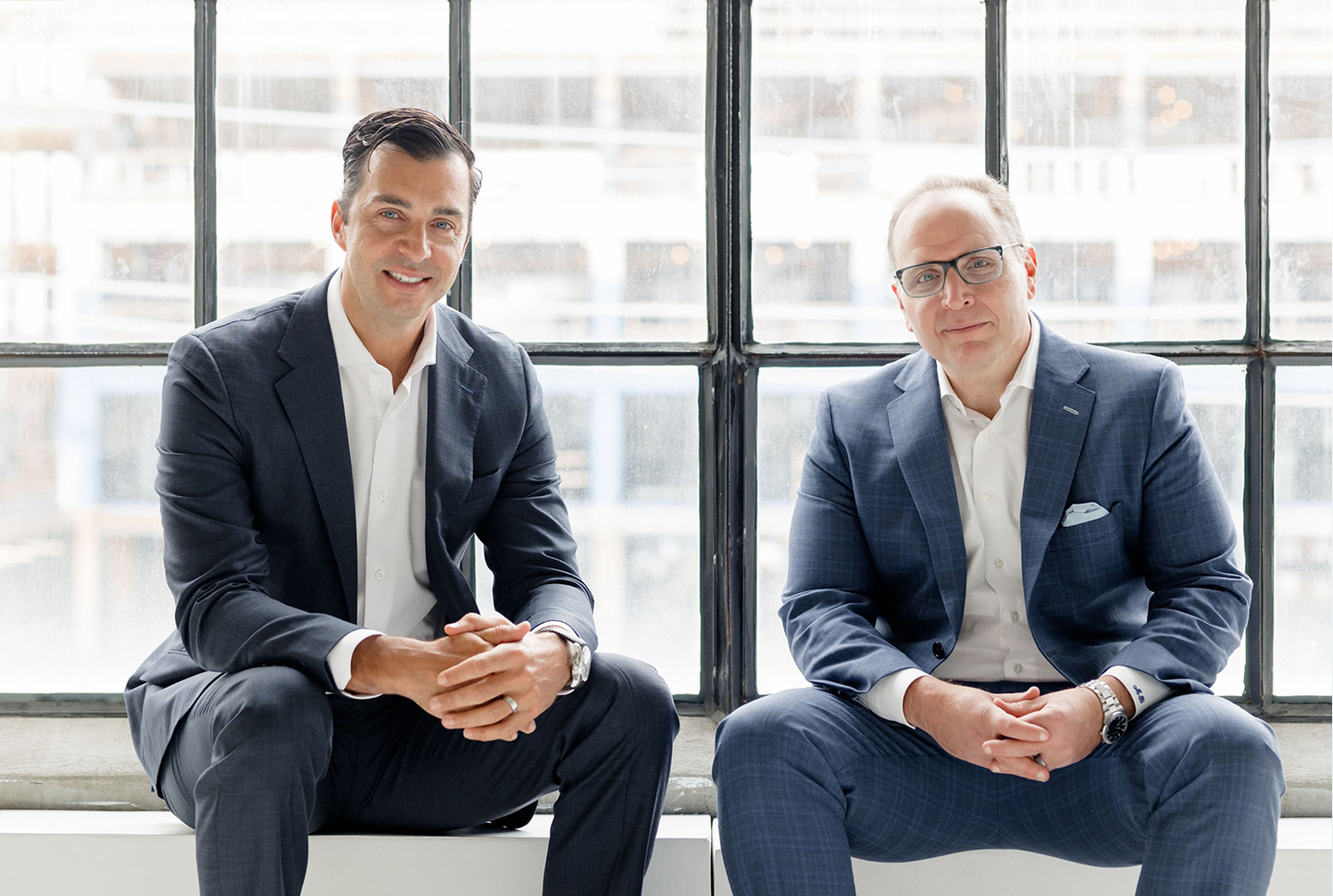 Jeffrey Wellwood and Matt Barasch sitting side by side on a window sill.