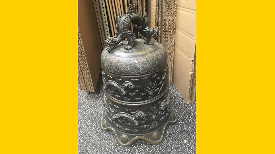 A heavy brass Chinese antique bell with depictions of Chinese dragons cast on the side. The top is adorned with a double-headed dragon that almost looks like a handle of the bell.