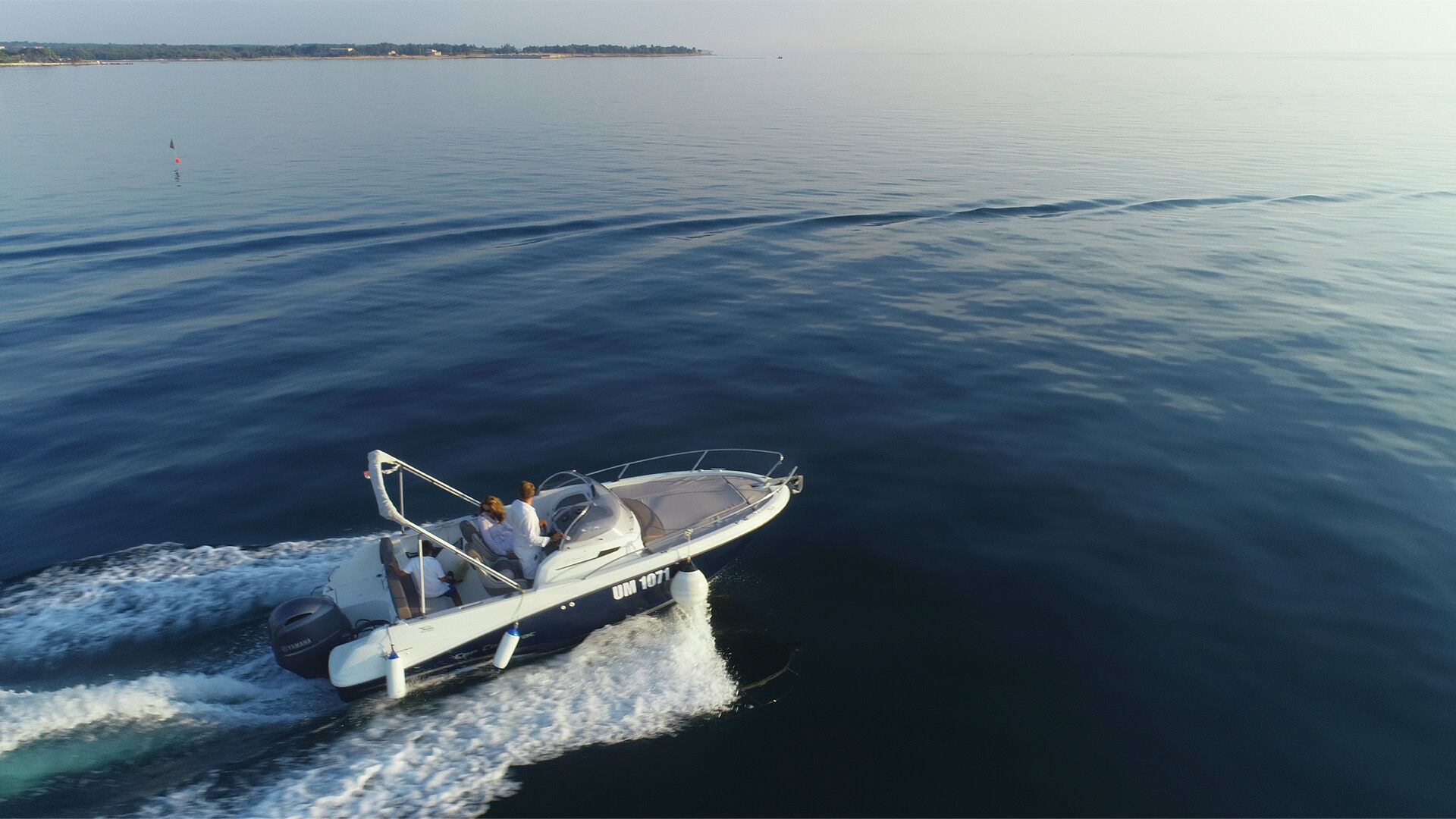 A boat going across very calm waters from the left to the right.