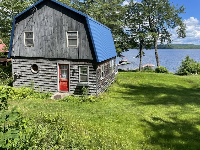 Residential home inspection of a lakeside cottage in Maine by Upfront Home Inspection & Maintenance. The property features weathered wood siding, a blue metal roof, and waterfront access.