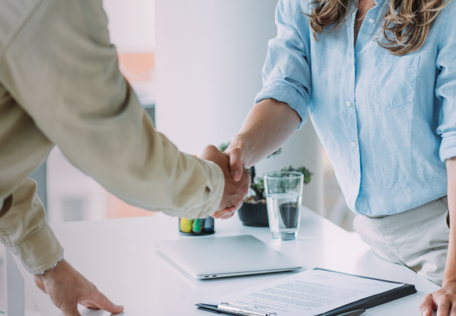 Two people shaking hands across a desk.