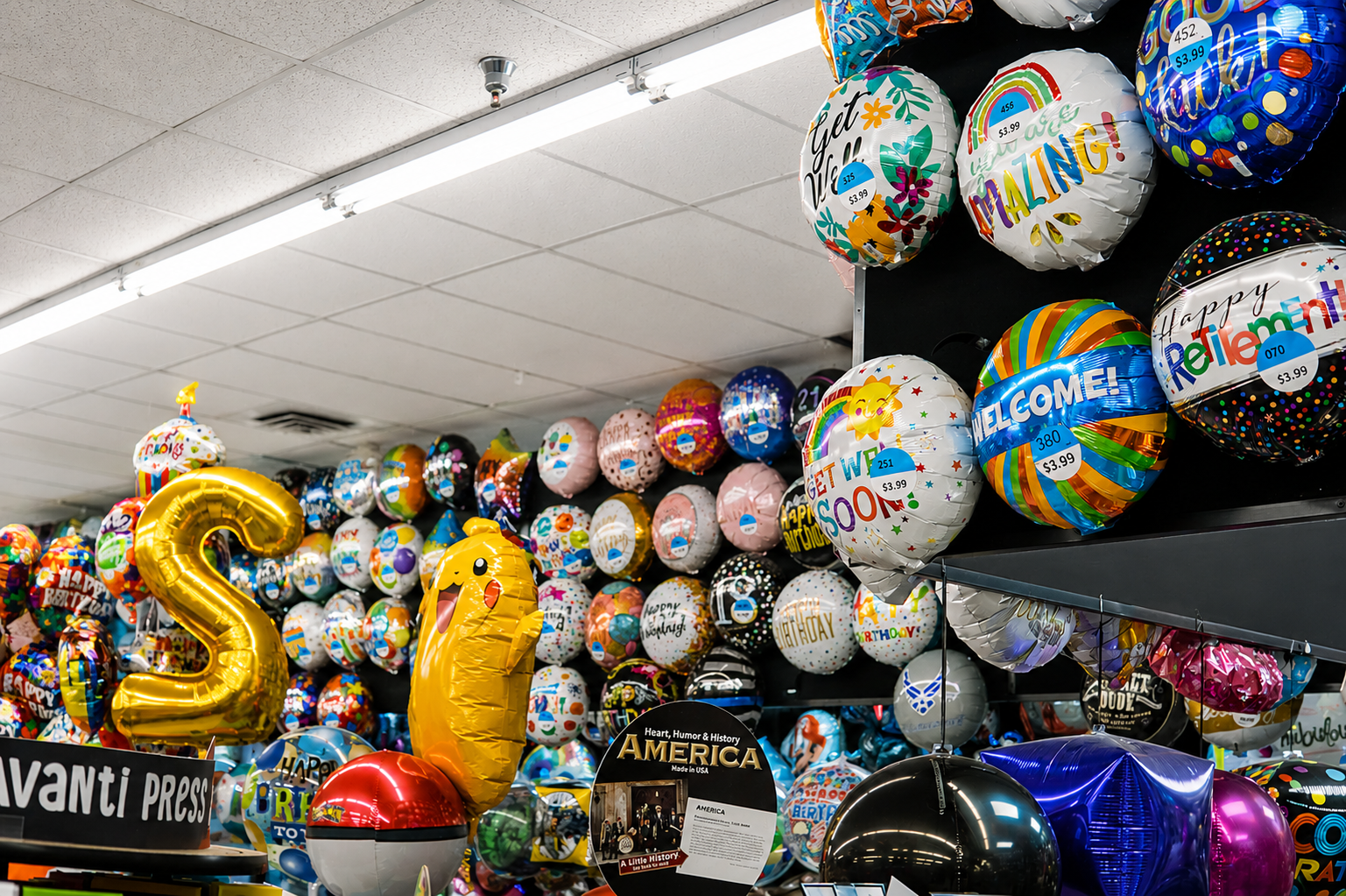 Colorful foil balloon display featuring birthday, graduation, retirement, welcome, and celebration-themed designs. A vibrant retail party supply section offering balloons for every special occasion.