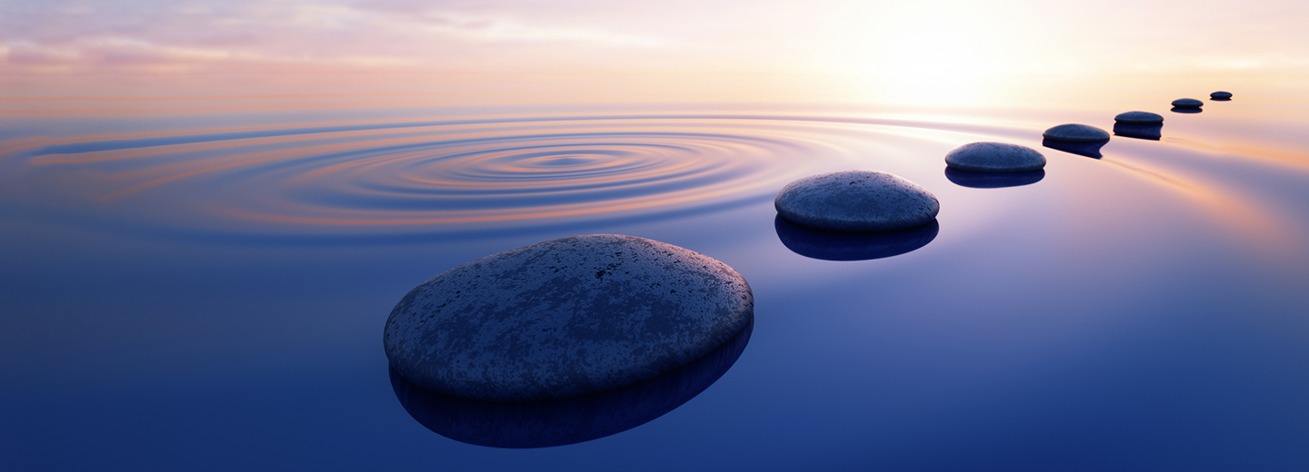 A path of smooth, round stones in a rippling lake under a pink and orange sky.