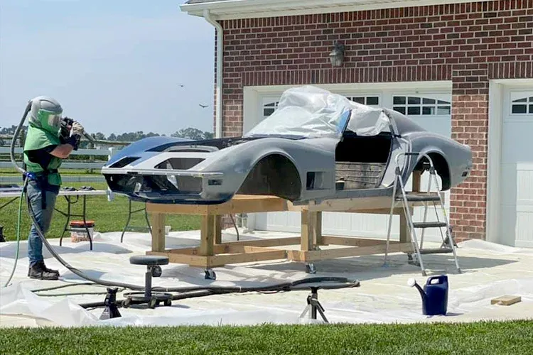 Technician sandblasting classic car body outdoors, removing old coatings and corrosion, preparing surface for restoration, ensuring clean finish and proper adhesion for repainting and protective coatings.