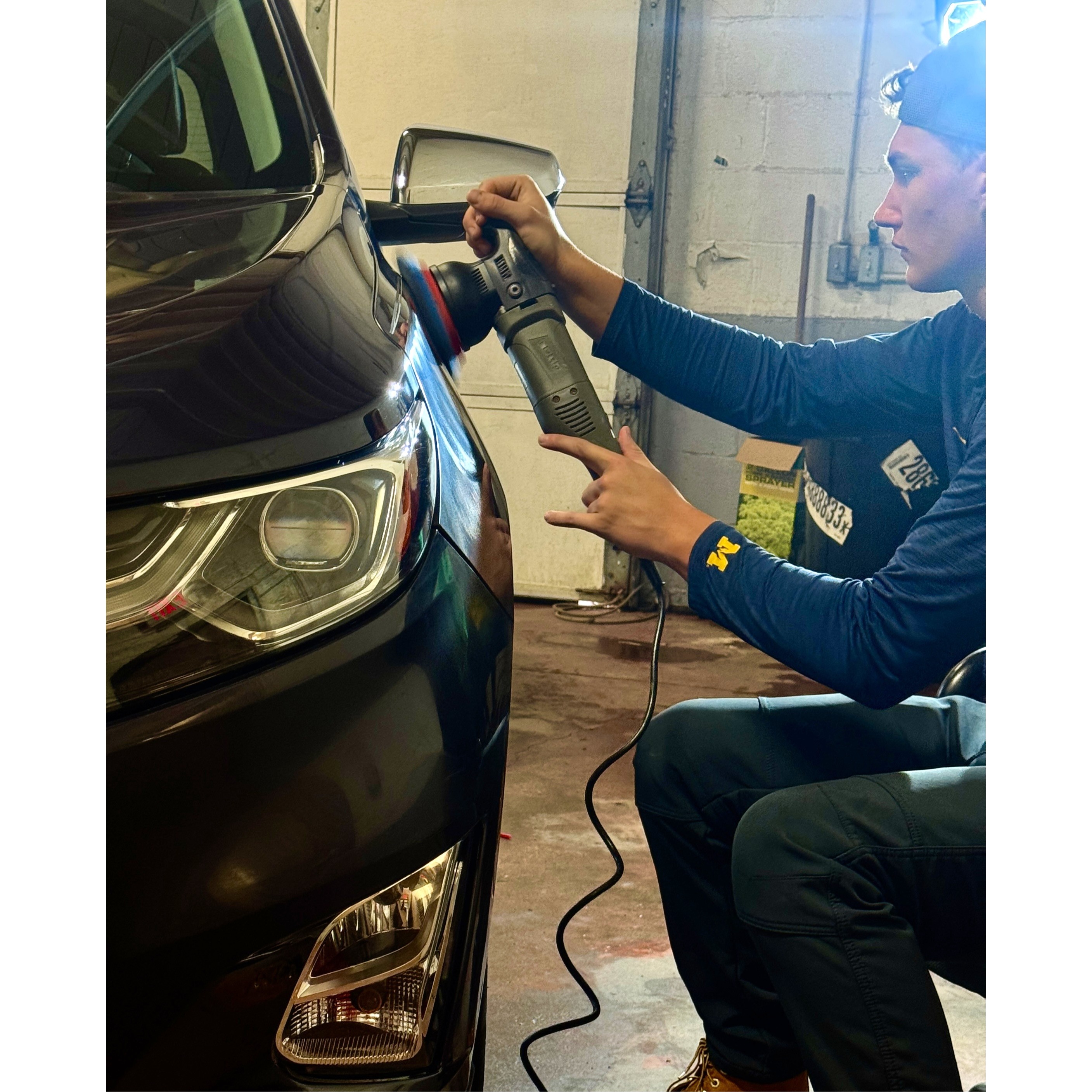 This image features a professional detailer at Refresh My Ride performing precision paint correction on a black vehicle using a high-speed orbital polisher. Working inside their dedicated auto detailing shop, the technician meticulously removes surface imperfections to restore a mirror-like finish and prepare the exterior for a long-lasting ceramic coating. This behind-the-scenes look highlights the expert craftsmanship and professional-grade equipment used by the team to serve car owners across Macomb and Oakland Counties.