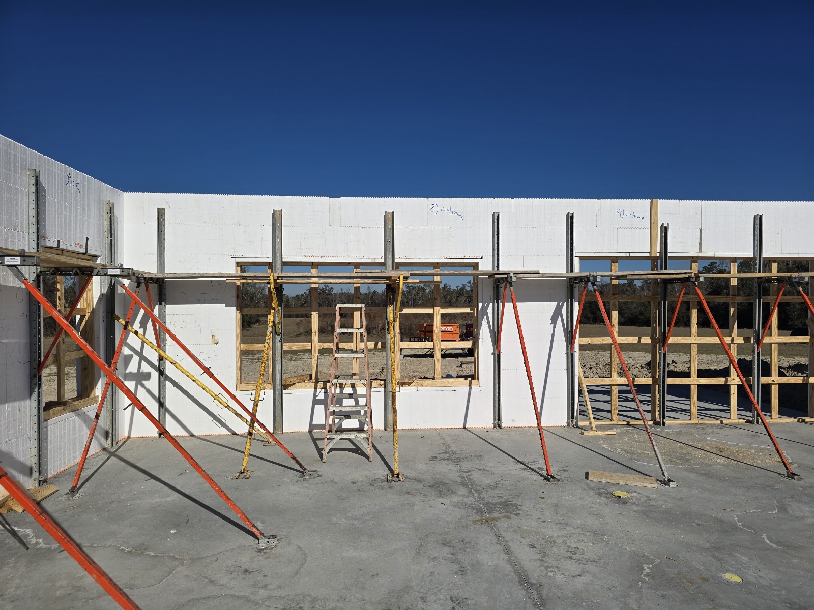 A construction site under a clear blue sky, featuring the partially built walls of a structure made  