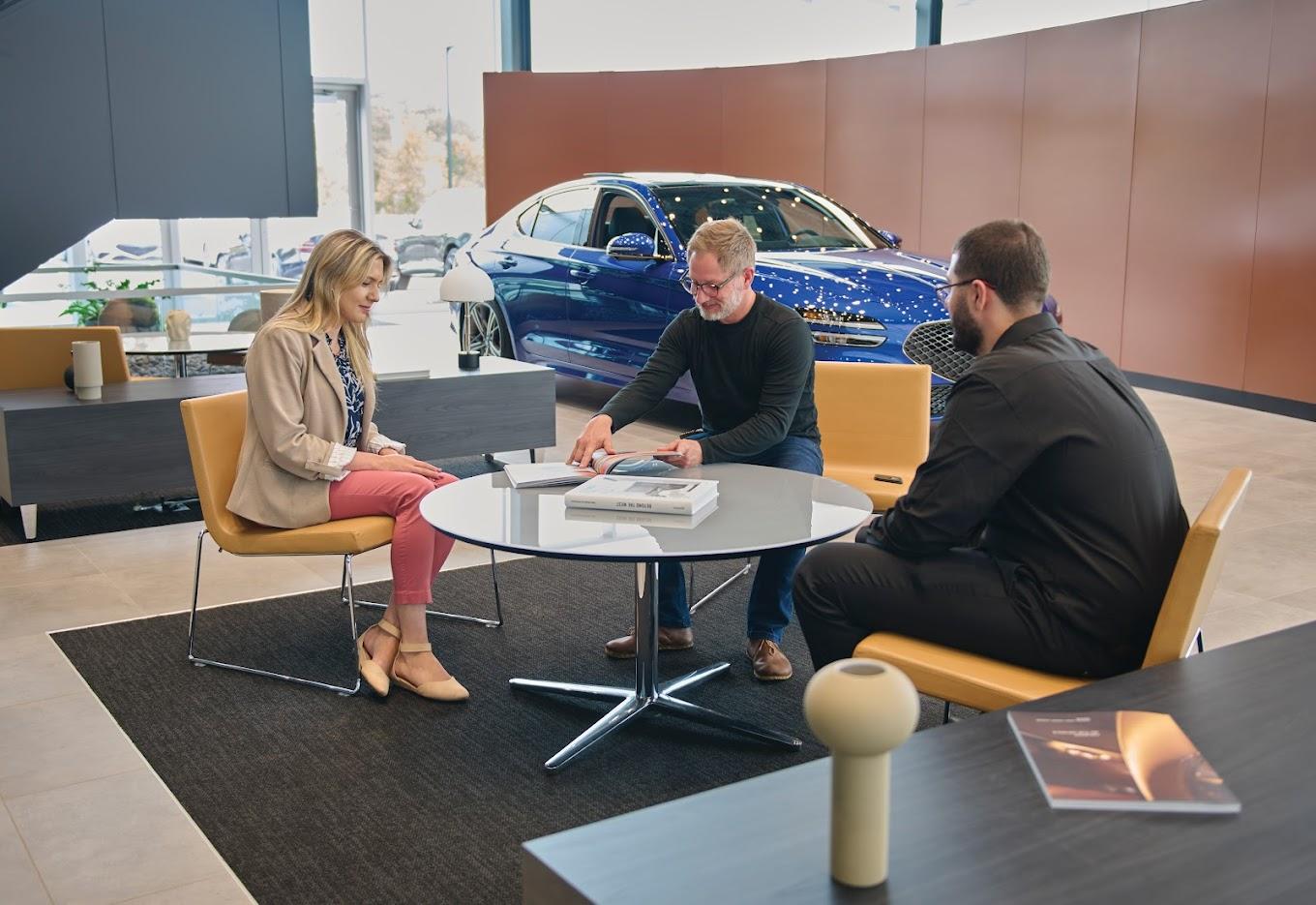 Three people meeting inside Genesis of Milford with a Genesis car in the background