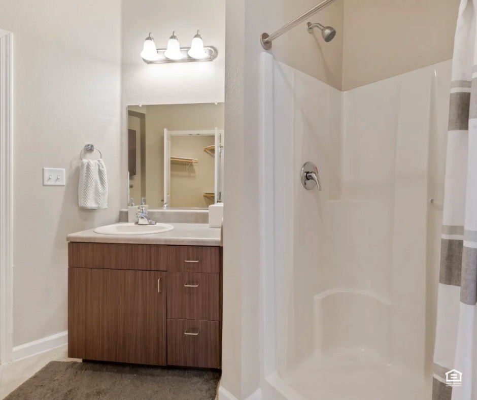 A clean and functional bathroom features a wood-grain vanity and a white walk-in shower.