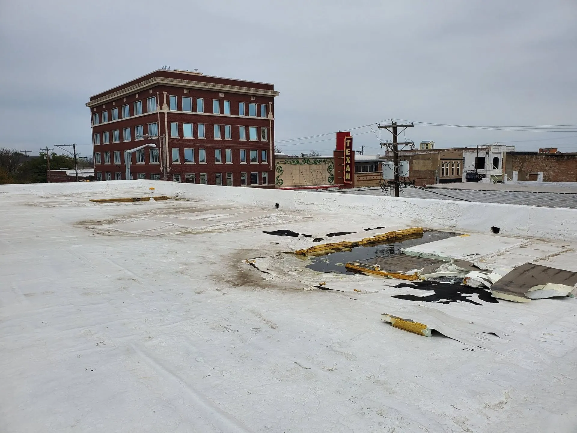 A commercial flat roof showing severe membrane failure, standing water, and deteriorated insulation  