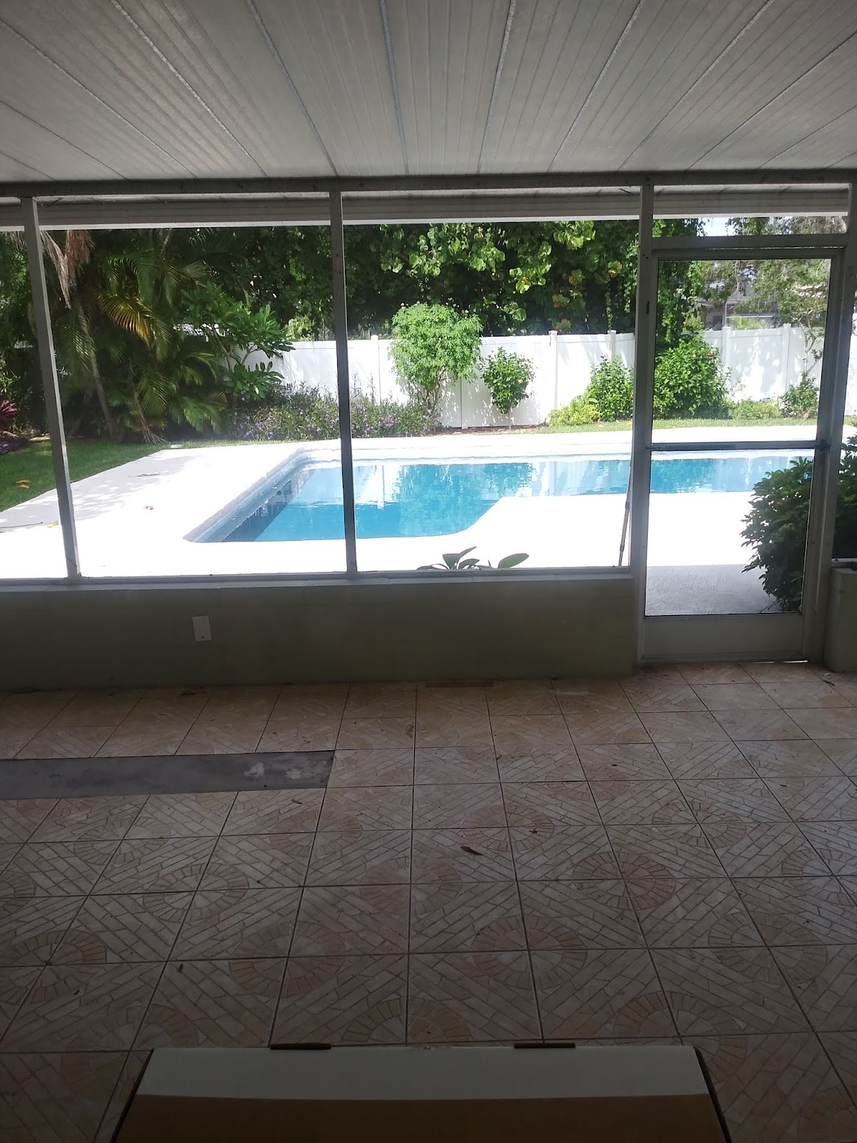 View from a covered patio overlooking a backyard swimming pool surrounded by tropical landscaping.