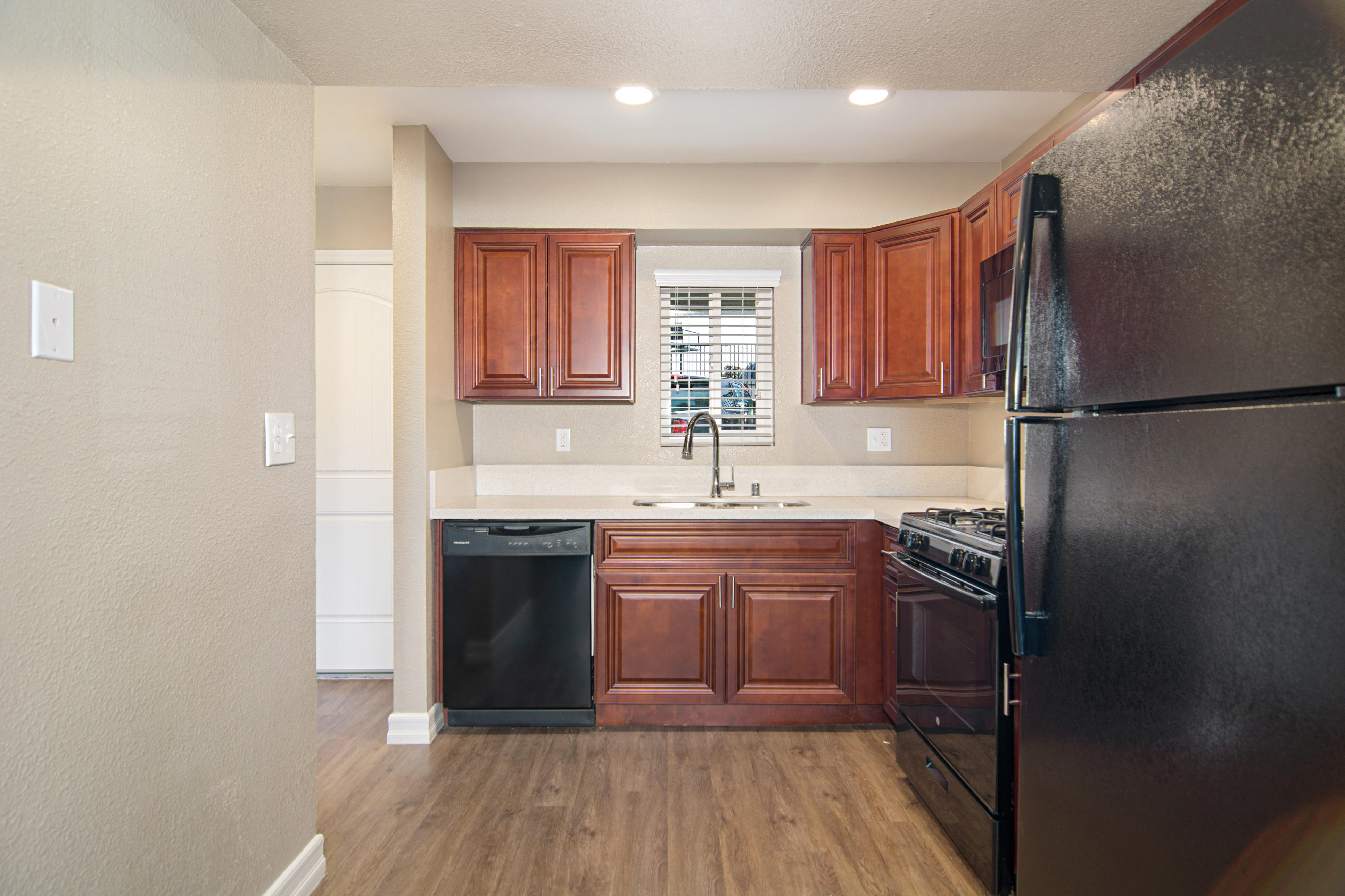 Kitchen with quartz counters, undermount sink, black appliances, and wood-style floors