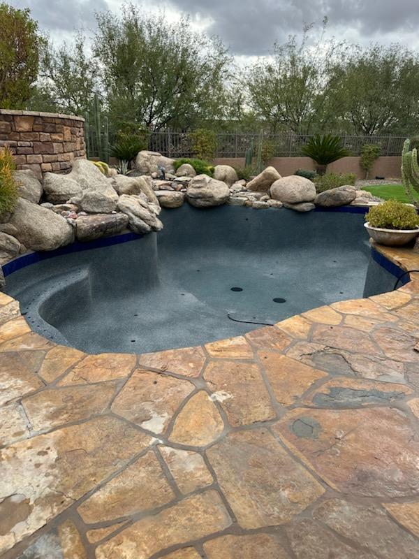 A finished natural-style swimming pool surrounded by large landscape boulders, stone decking, desert 