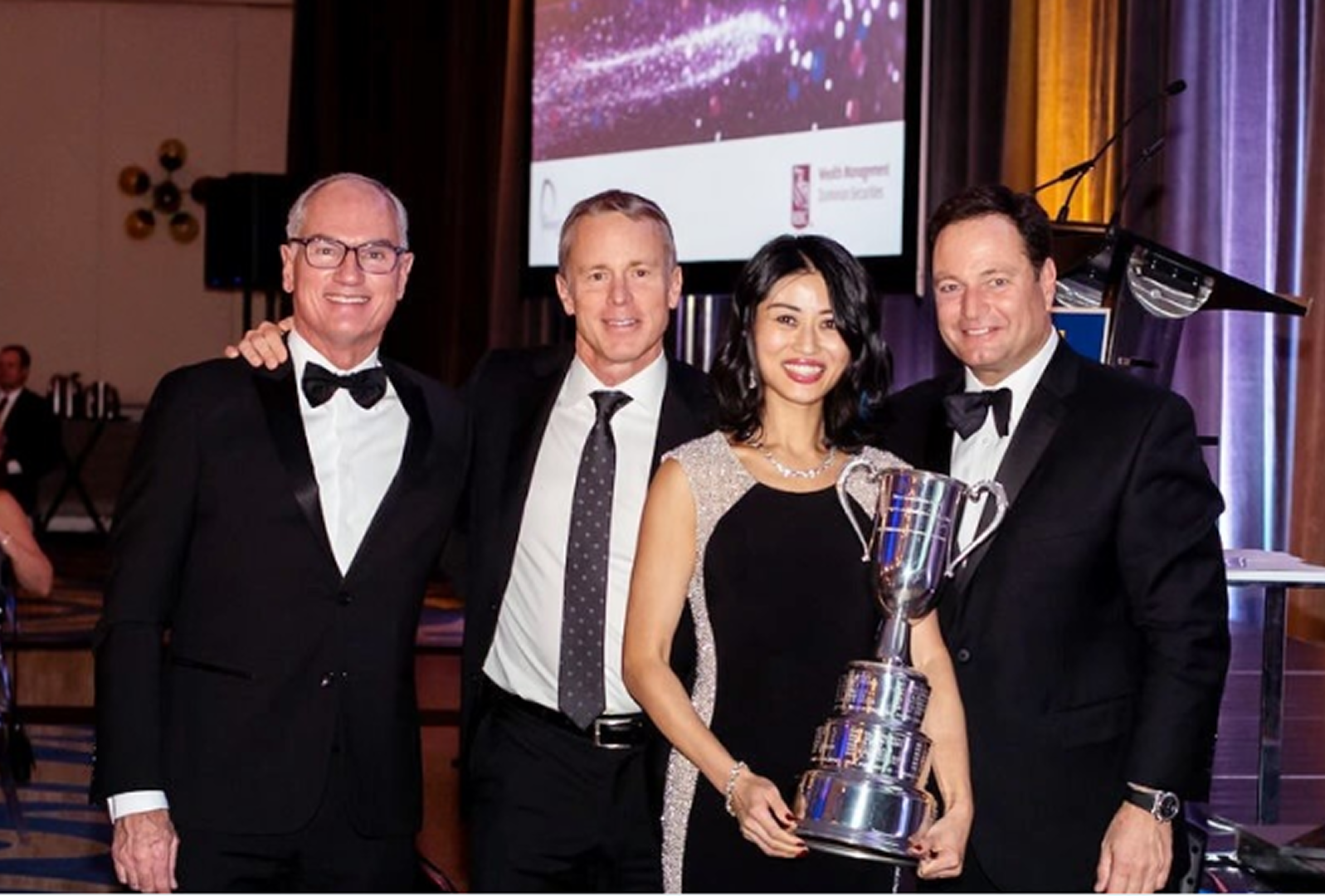 A group photo of Wendy Wen, holding a silver trophy, with three other members of the President's Club, dressed in black-tie attire.