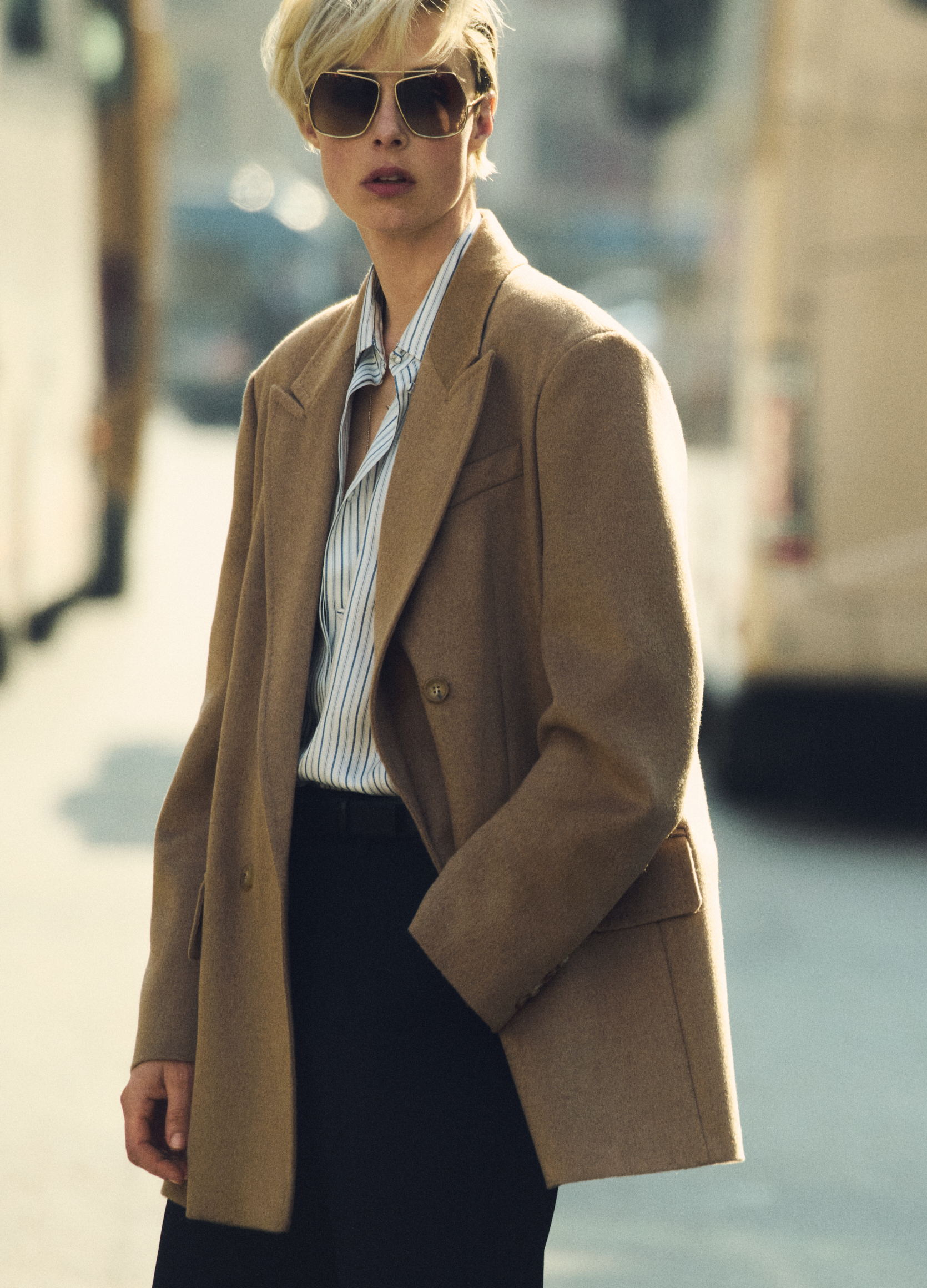 Modelka w dwurzędowej marynarce Olimpia Jacket Max Mara w kolorze wielbłądzim, z ciemnymi okularami i koszulą w miejskiej scenerii.