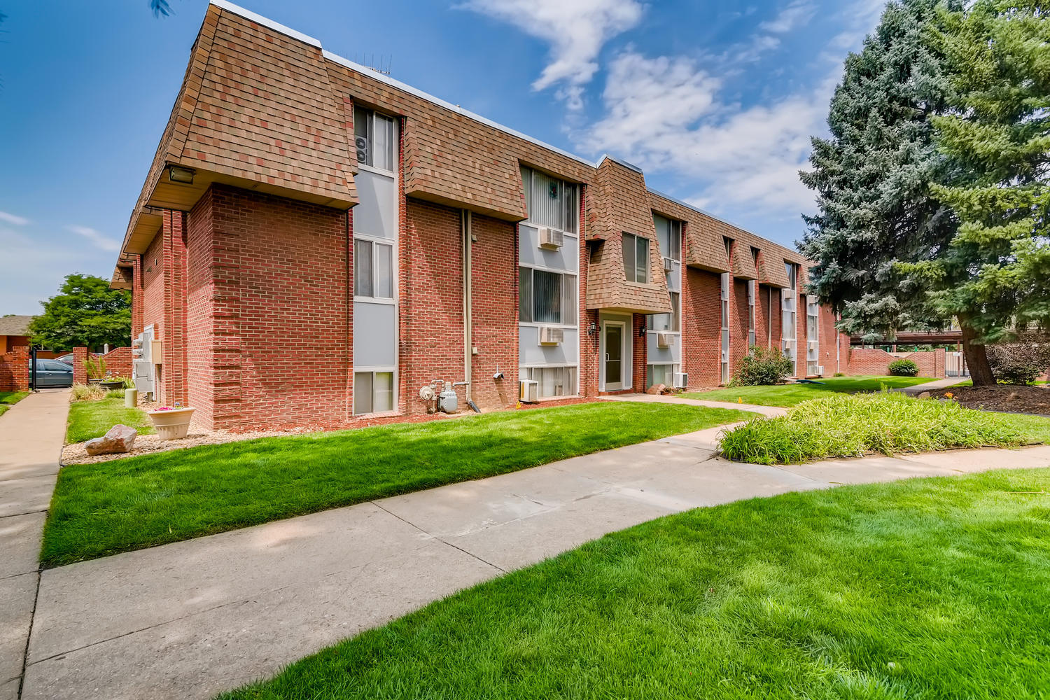 Brick and siding building exterior with concrete sidewalk and green grass lawn.