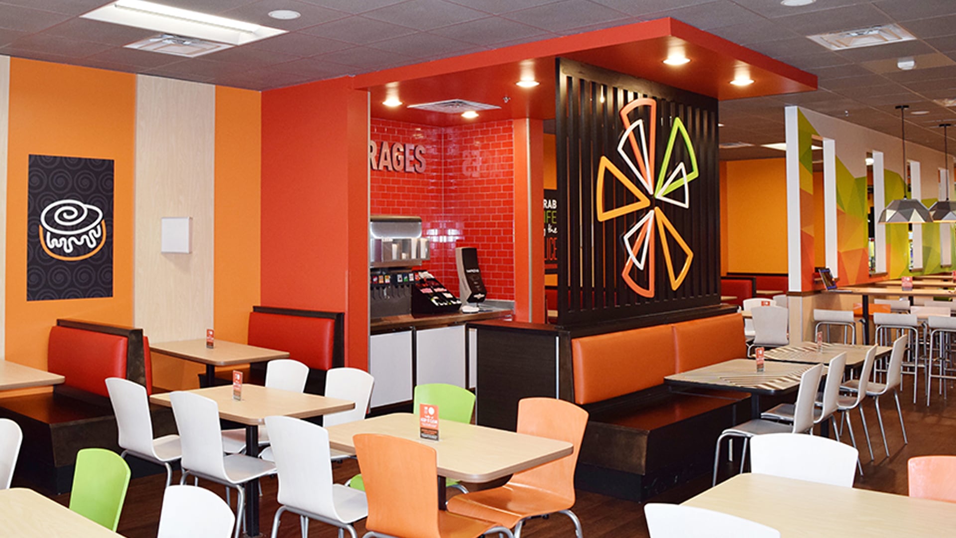 The inside of a Cicis dining room with a mix of brightly coloured chairs in front of small tables and plush red booths in against the wall.