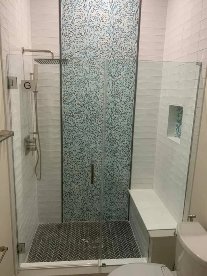 A modern bathroom with a glass-enclosed shower featuring a decorative tiled back wall and a built-in bench, alongside a white toilet.