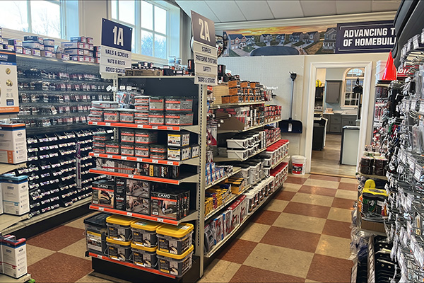 Store aisles at Builders FirstSource New Bedford displaying hand tools, cleaners, caulking, and painting supplies with clear signage.