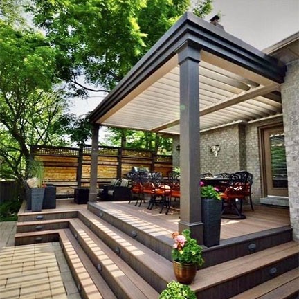 Black-frame motorized louvered pergola over a multi-level wood deck with outdoor dining and integrated step lighting