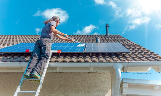 Residential solar panel cleaning being performed from a ladder at the roofline, illustrating hands-on maintenance of a rooftop photovoltaic system.