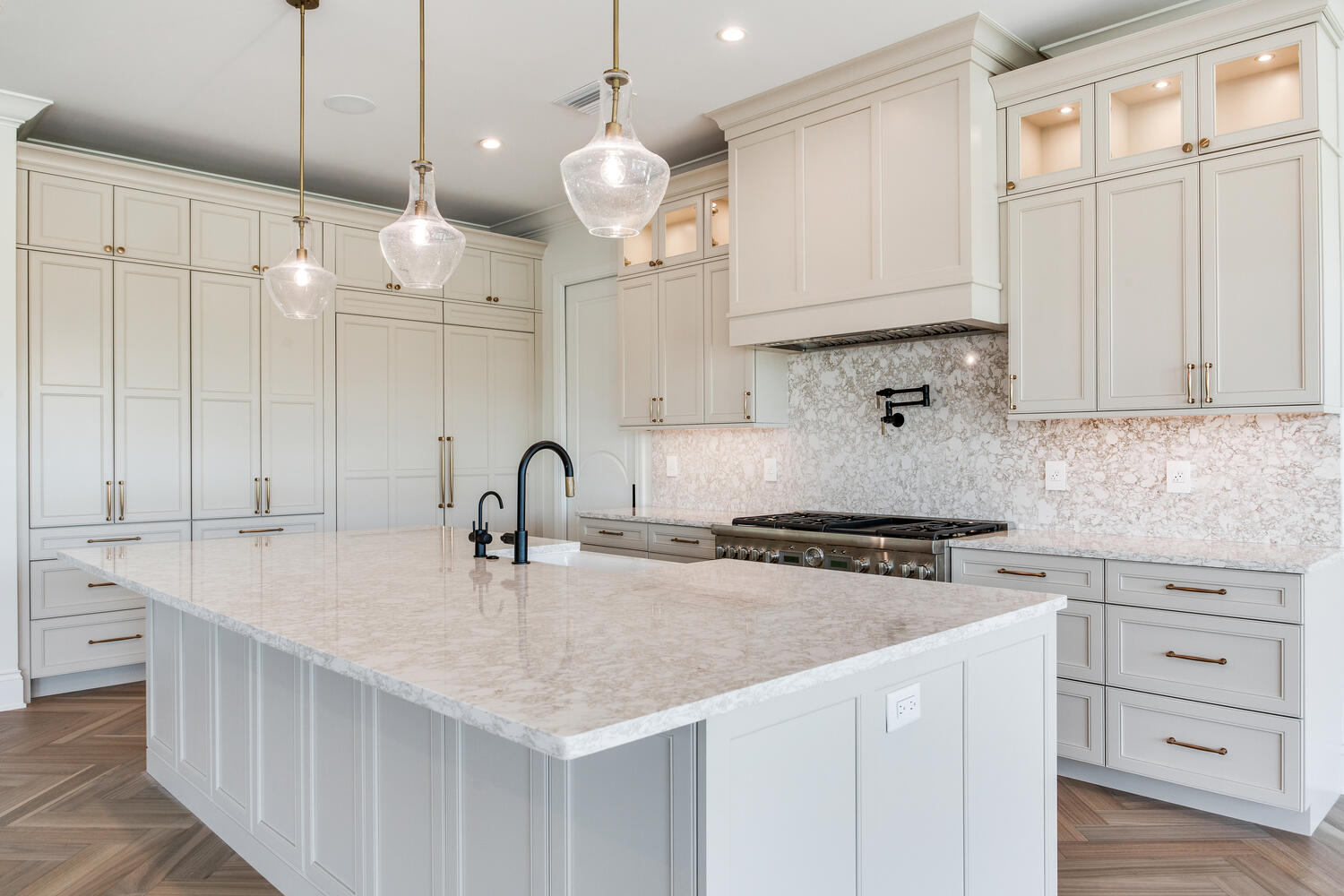 Elegant custom kitchen featuring a large waterfall island, white cabinetry, chandelier-style pendant lighting, and upscale modern finishes.