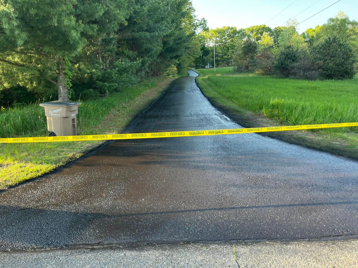 Asphalt driveway undergoing sealcoating treatment with caution tape, enhancing pavement protection, durability, and long-term appearance.