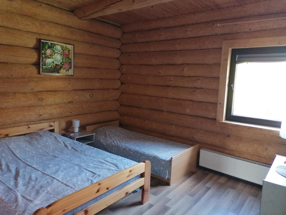 Gaiša un mājīga guļamistaba viesu namā 'Palmas' ar komfortablu gultu, koka detaļām un logu ar skatu uz dabu.