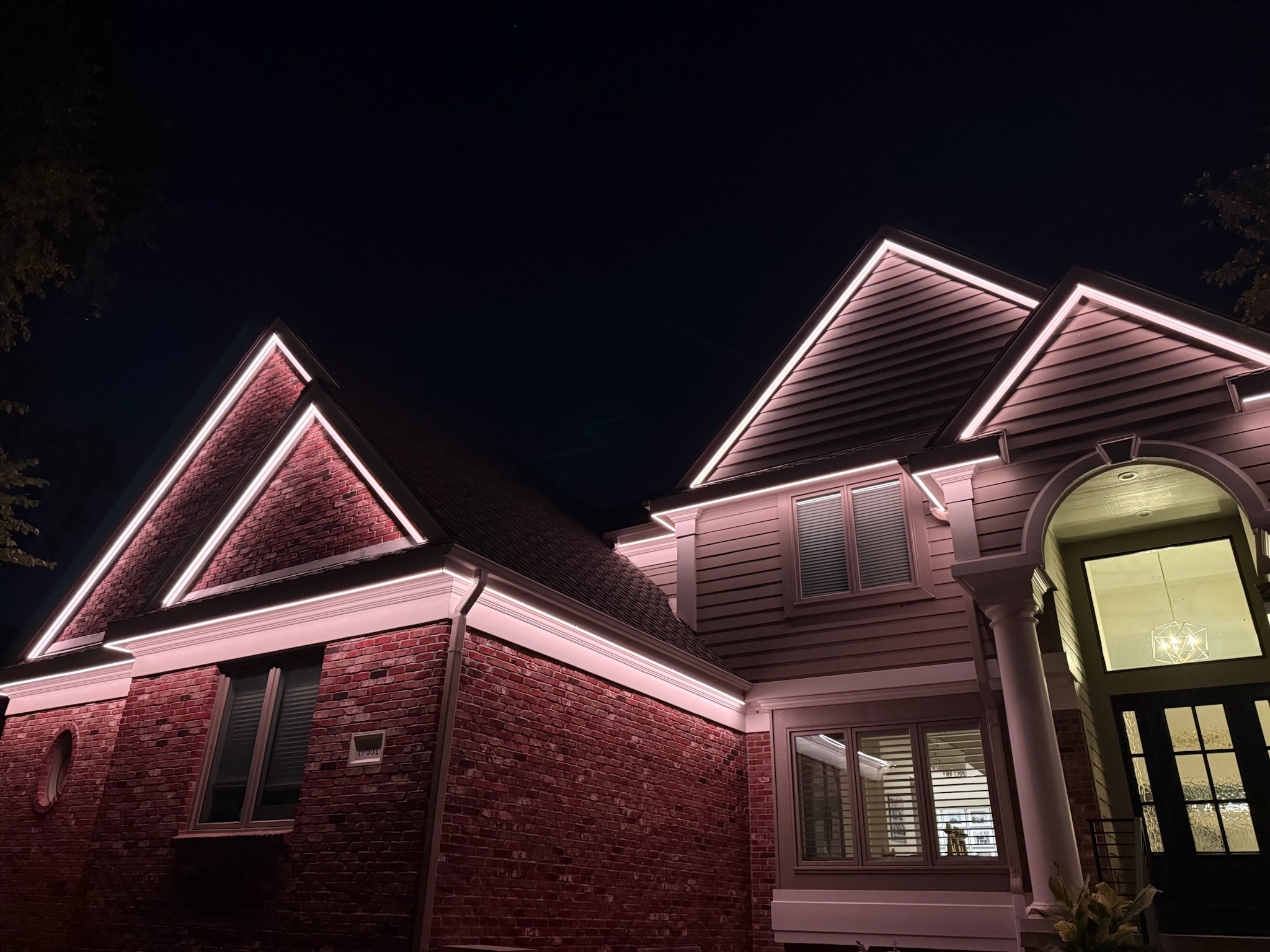 Residential roofline lighting installation highlighting the architectural peaks and entryway of a home at night.