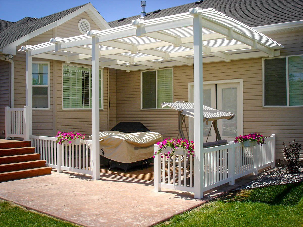 Create a charming and shaded backyard retreat with a custom vinyl pergola from DeckPro LLC. This project in Rexburg, Idaho, features an attached pergola design that provides filtered shade over the patio. The installation includes a matching white vinyl railing system with integrated flower boxes, combining beauty, function, and maintenance-free durability for the ultimate outdoor living space.