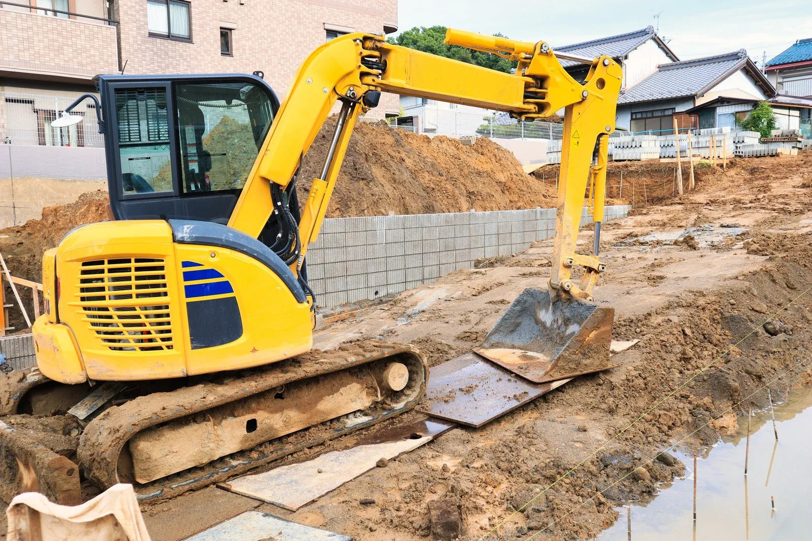 Yellow excavator performing excavation and grading work on a residential construction site. Heavy equipment prepares the land for foundation installation, utility trenching, drainage systems, and professional site development with precision earthmoving and soil preparation services.